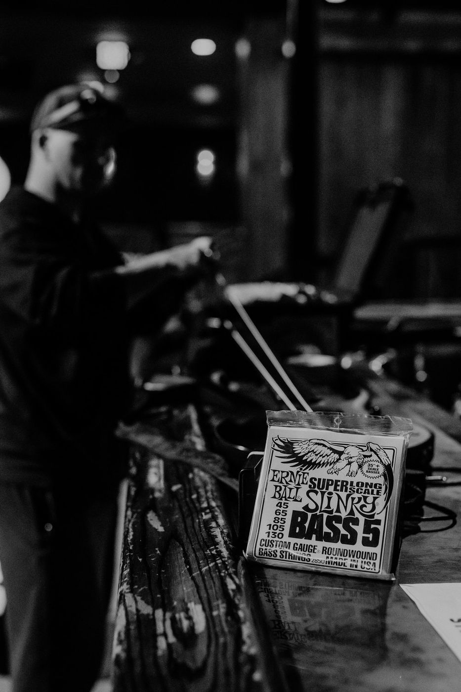 A pack of Ernie Ball Super Long Scale Slinky Bass 5 strings on the bar, tech working behind